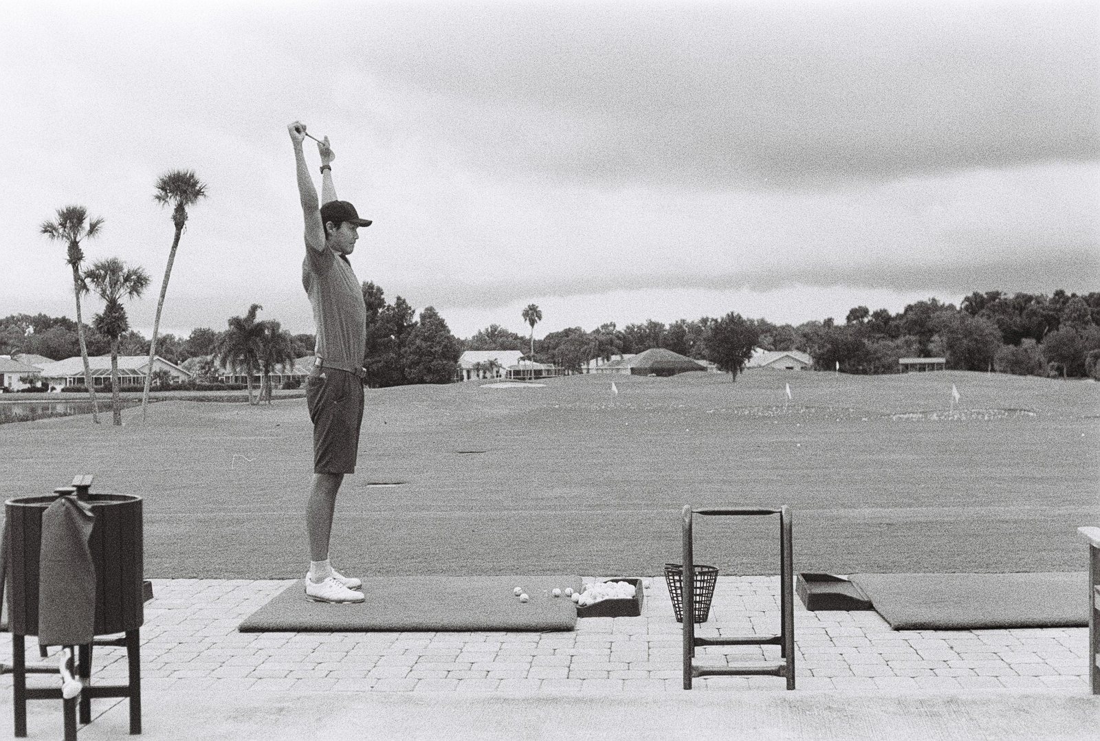 Black-and-white film photo of Nurtai stretching with a club overhead on the range