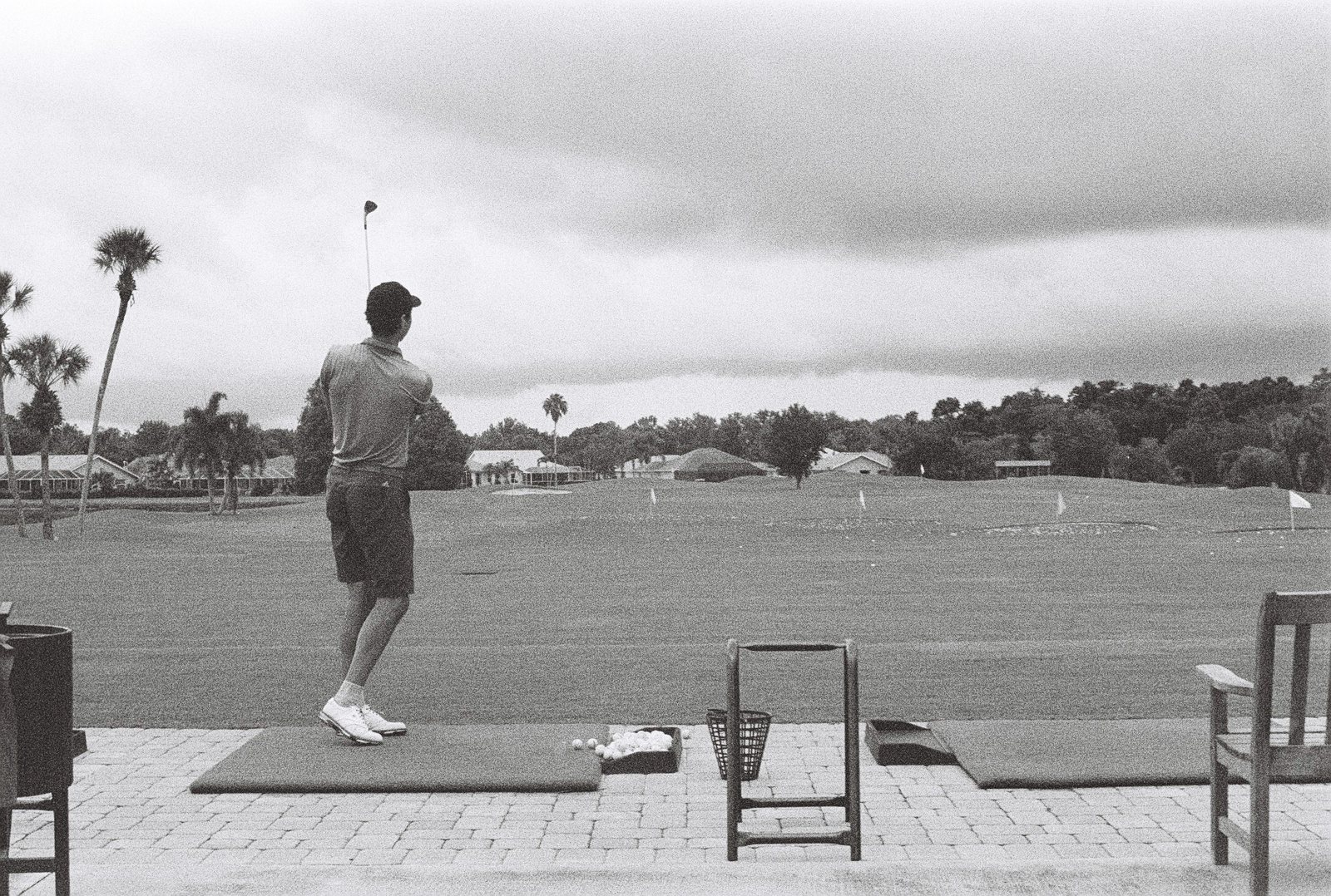 Black-and-white film photo of Nurtai finishing a swing on a Florida driving range