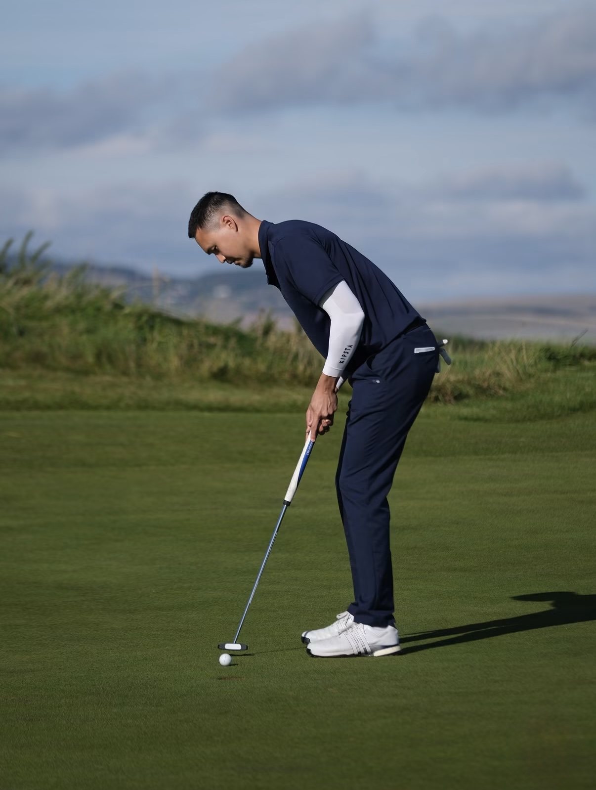Nurtai lining up a putt on a links green with dunes behind